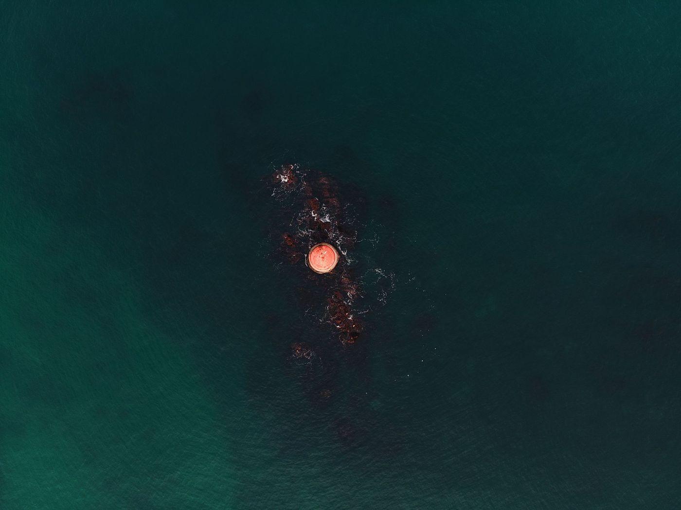 A single monitoring buoy floating in calm ocean water, seen from directly above